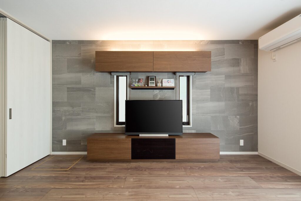 TVの背面壁はグレーのエコカラ ットで演出。間接照明を入れるこ とで、エコカラットが映えるよう にしている。2つの縦長のスリッ ト窓も壁面のアクセントに。